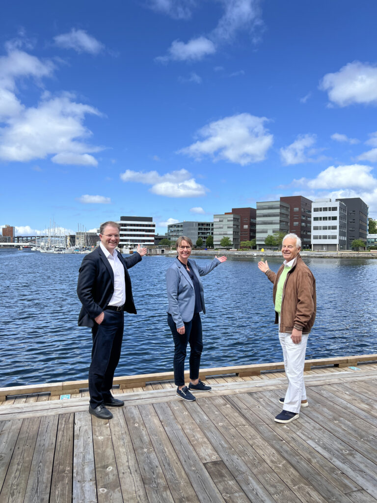 Tor Instanes, Bodil Valland Steinhaug og Bjart Nygaard står på bryggen i Solheimsviken og viser hvor seniorboligene vil bygges på Marineholmen i Innovasjonsdistriktet.